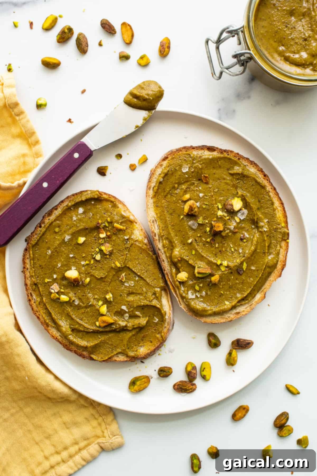Homemade pistachio butter spread generously on a piece of toasted bread, garnished with fresh fruit.