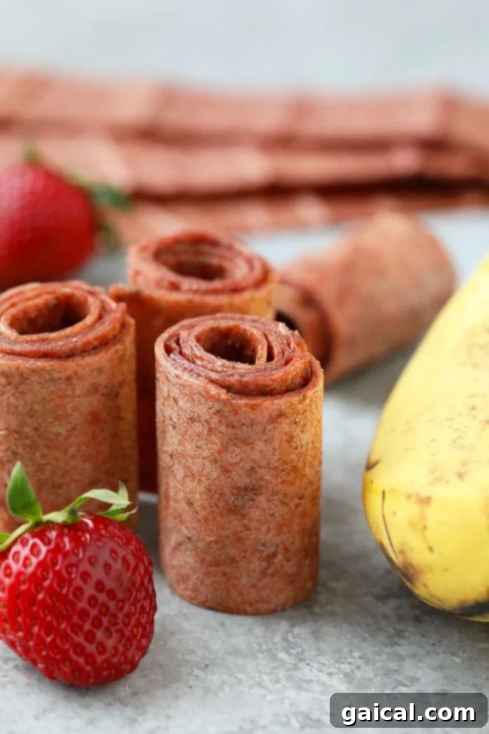 Sun-Kissed Strawberry Banana Fruit Leather 2 Rolled fruit leather strips, showcasing the delicious strawberry banana flavor, with fresh fruit in the background.