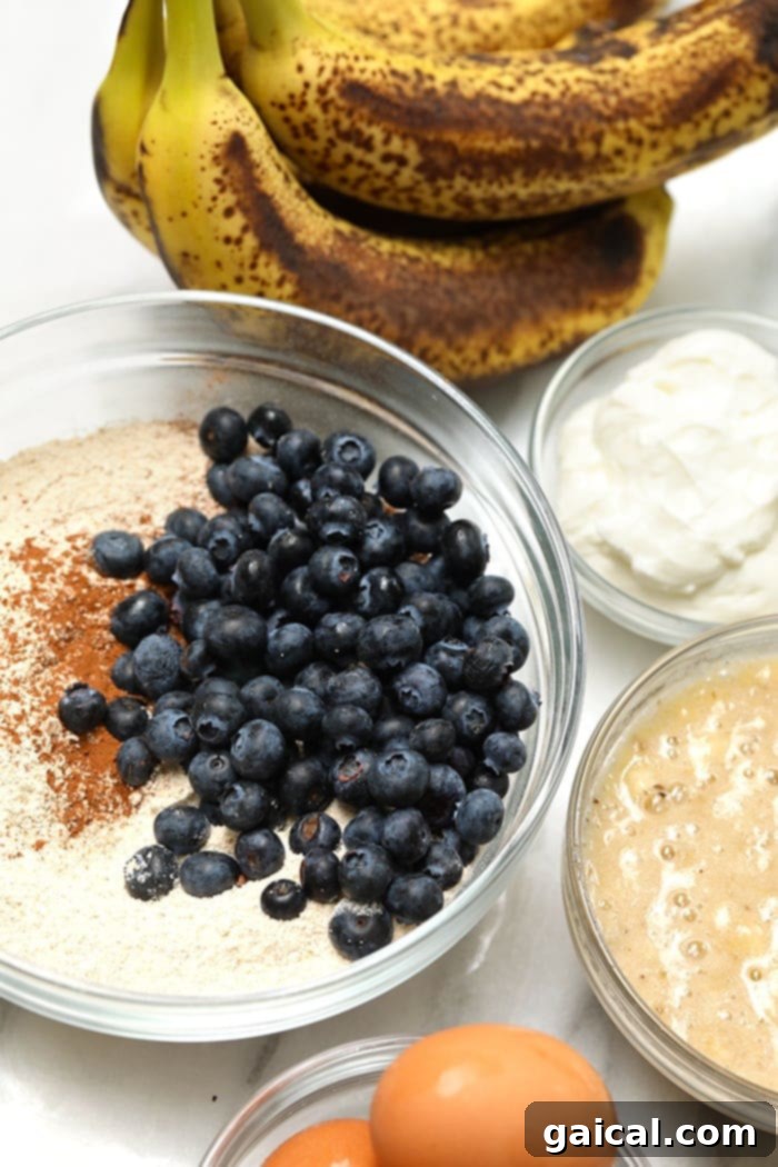 This healthy blueberry banana bread is an easy breakfast that the whole family will love! It is naturally sweetened, delicious and you just can’t beat moist banana bread. Make a loaf today! A collection of fresh ingredients for baking blueberry banana bread, including bananas, blueberries, flour, and a mixing bowl, laid out on a kitchen counter.