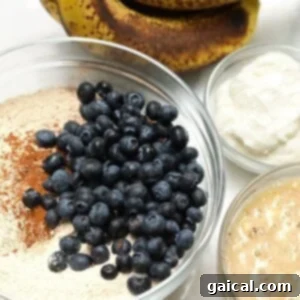 A table topped with bowls of various food ingredients, including ripe bananas and blueberries, ready for baking this healthy banana bread.