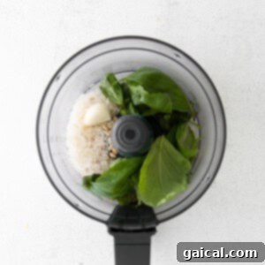 A food processor filled with fresh basil, garlic, and pine nuts, ready for blending into pesto.