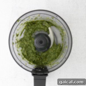 Basil pesto being blended in a food processor, showing its developing texture.