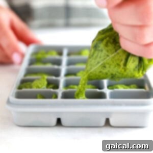 Fresh Basil Pesto Made Easy 7 A person preparing homemade pesto by pouring it into a reusable silicone ice cube tray for easy freezing and portioning.