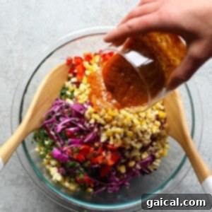 A person gently mixing the colorful ingredients of Thai Chili Corn Salad in a large bowl, ensuring the dressing coats every vegetable.