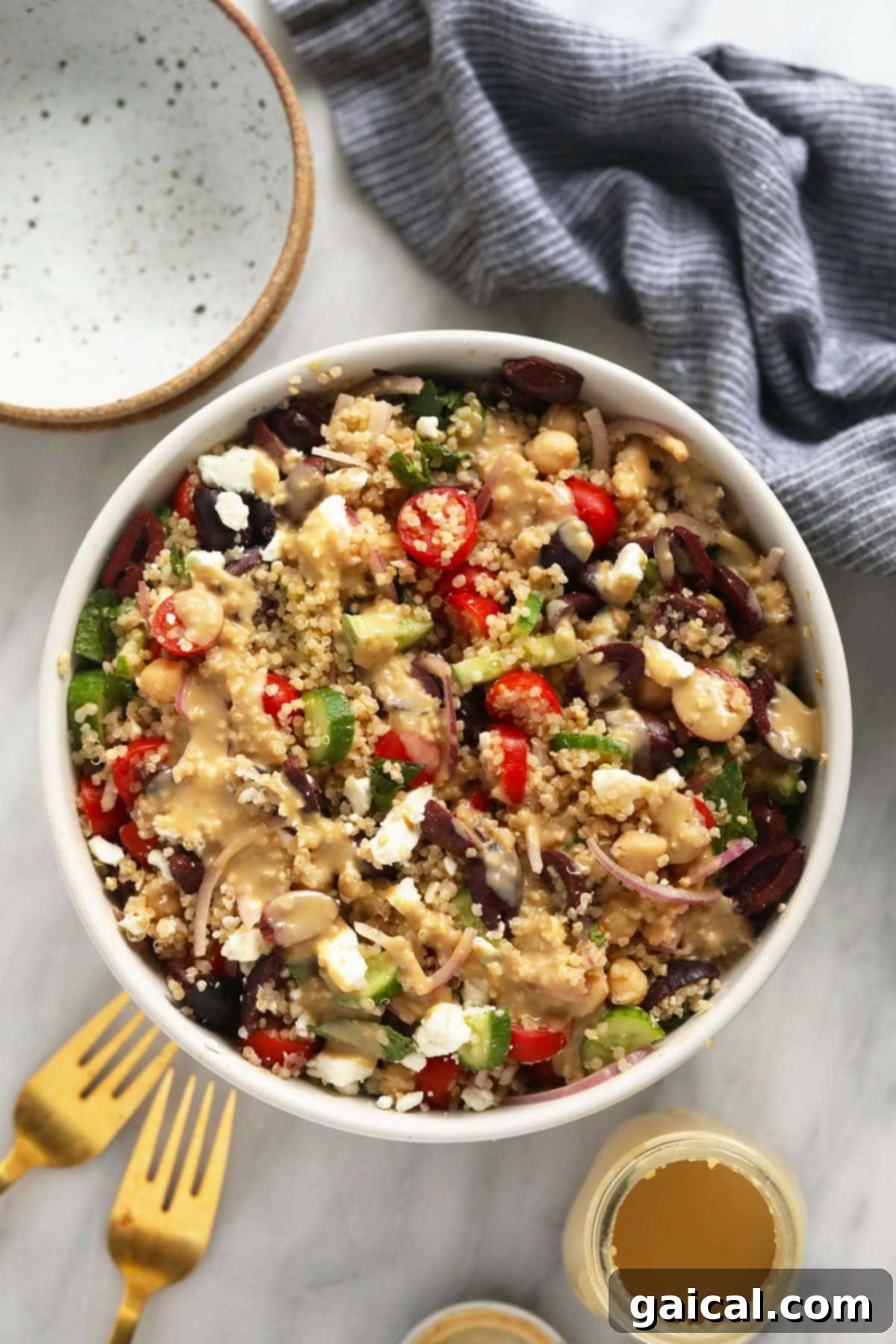 Mediterranean Quinoa Salad with Hummus Dressing - Healthy & Delicious A vibrant Mediterranean Quinoa Salad in a bowl, drizzled with creamy hummus dressing.