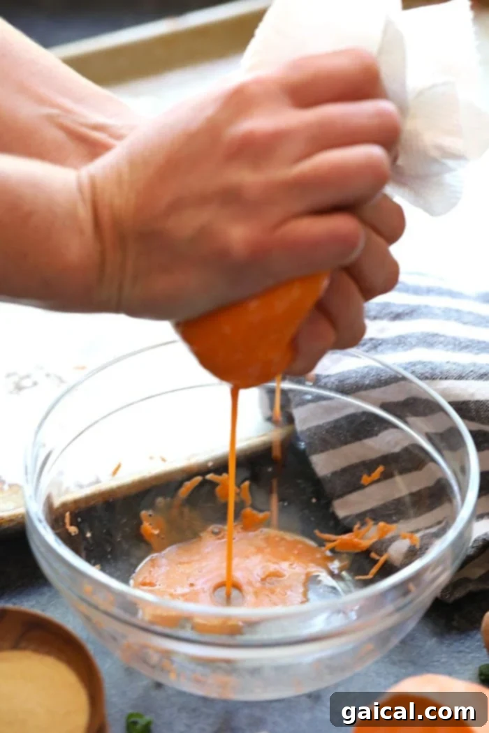 Grate up some sweet potatoes and make these baked sweet potato tater tots. They are a healthy and delicious spin on a classic! A close-up shot of hands squeezing liquid out of grated sweet potatoes using a tea towel, a crucial step for crispy tots.