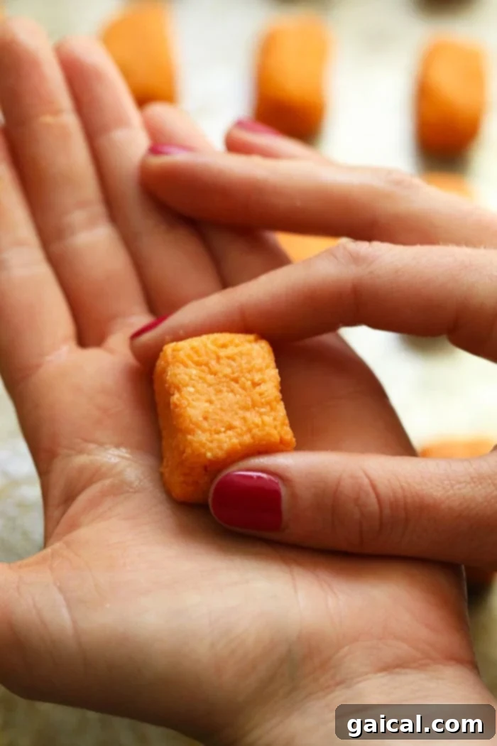 Making homemade sweet potatoes is very easy! They are ready in less than an hour and absolutely delicious! Hands carefully forming a small tater tot from the sweet potato mixture on a baking sheet, demonstrating the shaping process.