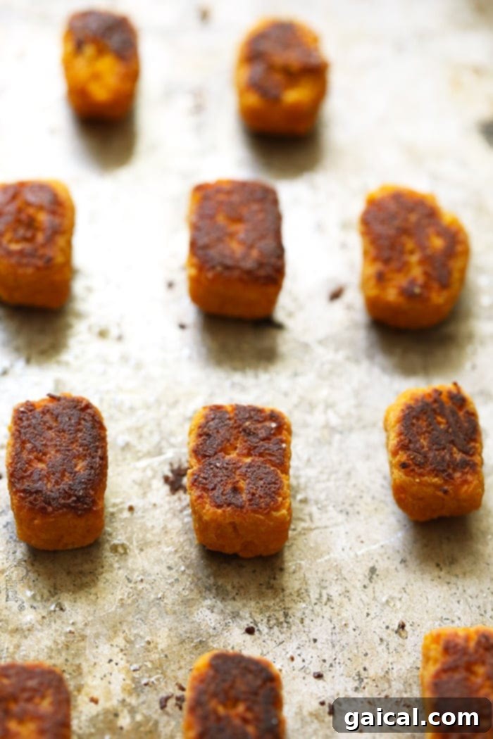 Baked Sweet Potato Tater Tots are crunchy and delicious! Make your favorite sauce for a healthy appetizer or side dish. YUM Freshly baked sweet potato tater tots cooling on a baking sheet, golden and perfectly crispy.