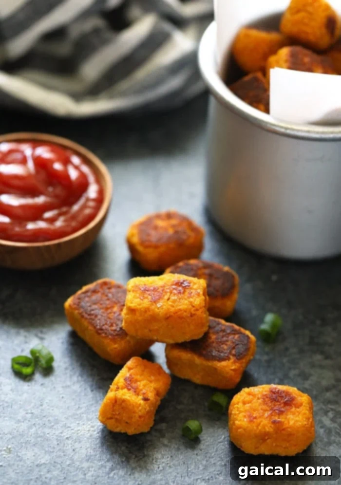 Make these sweet potato tater tots for a healthy and delicious side dish this week! They are made with grated sweet potato and almond flour. Did I mention that they are VEGAN!? A vibrant stack of baked sweet potato tater tots on a white plate, showcasing their perfect golden texture.