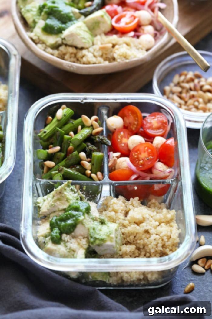 Pesto chicken meal prep container with perfectly organized components: chicken, asparagus, quinoa, and salad.
