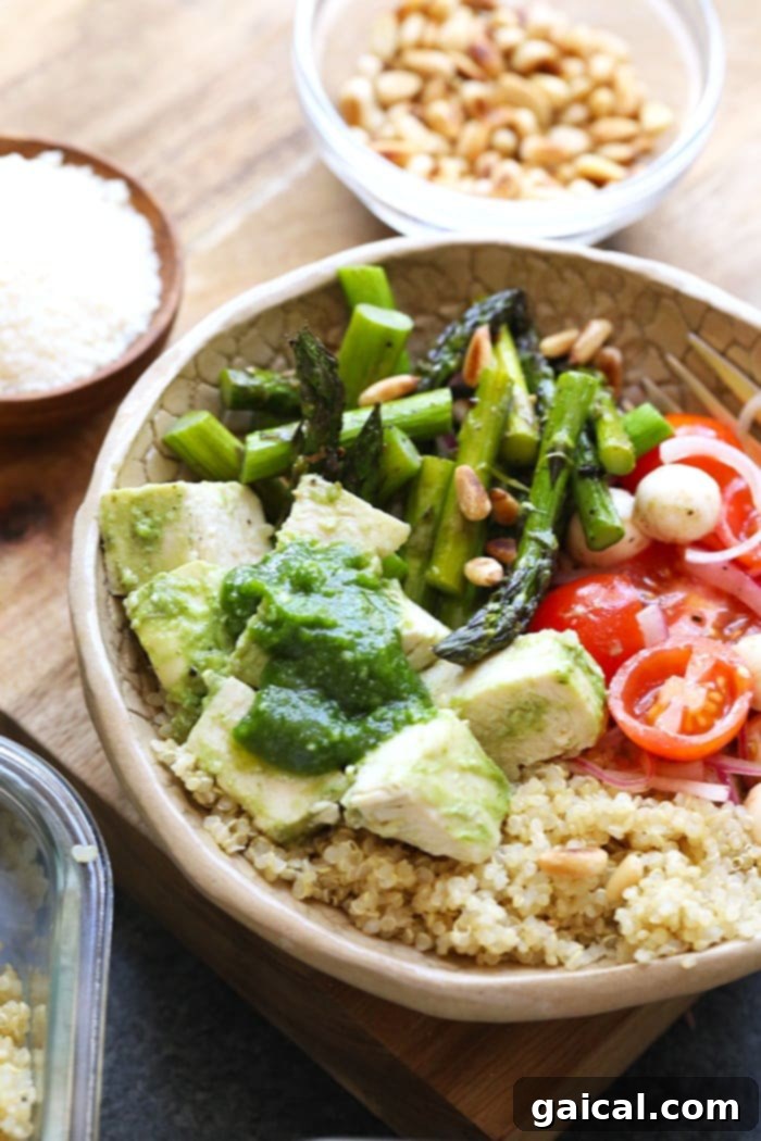 Pesto chicken, roasted asparagus, quinoa, and a fresh mozzarella-tomato salad beautifully presented in a serving bowl.