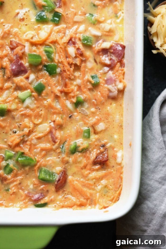 Sweet Potato Hash Breakfast Casserole Pre-Bake Unbaked breakfast casserole mixture in a glass baking dish, showing raw eggs mixed with sweet potato, bacon, and vegetables.