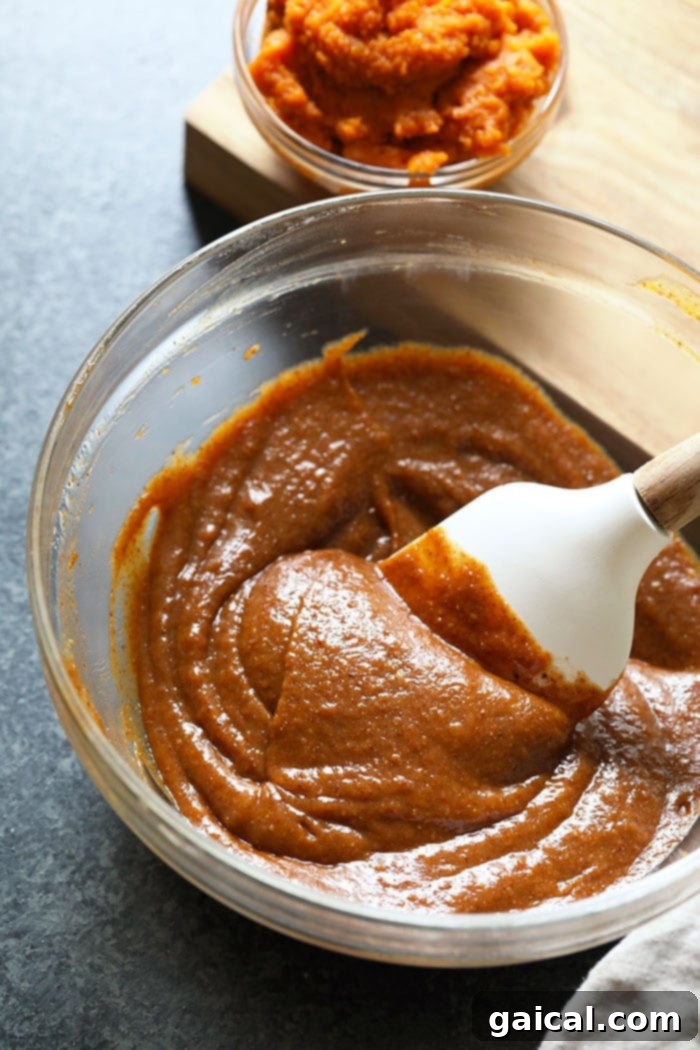 A selection of natural and wholesome ingredients for healthy pumpkin freezer fudge beautifully laid out on a kitchen counter: a jar of almond butter, solid coconut oil, a can of pumpkin puree, pure maple syrup, and a small bowl of ground cinnamon.