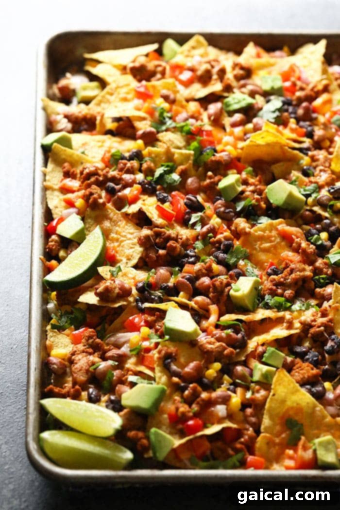 Loaded Baked Chicken Nachos 2 Golden brown baked chicken nachos on a baking sheet, loaded with melted cheese and fresh toppings, ready to serve.