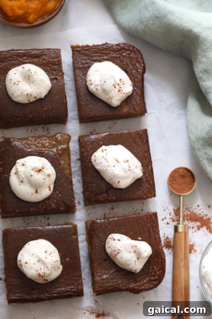 Wholesome Pumpkin Spice Bars 6 Several healthy pumpkin pie bars, each topped with a swirl of whipped cream, arranged appealingly on a platter.