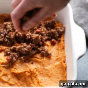 A person preparing a healthy sweet potato casserole by scooping mashed sweet potatoes into a dish.
