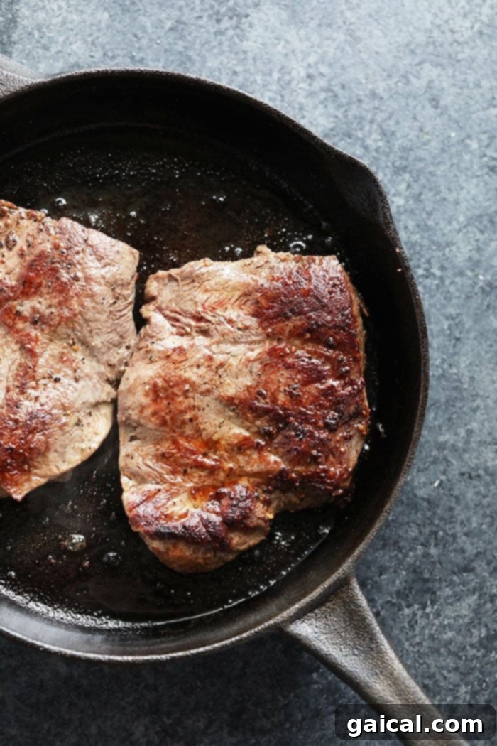 Close-up of a skillet with thinly sliced, seared flank steak, showing its tender texture.
