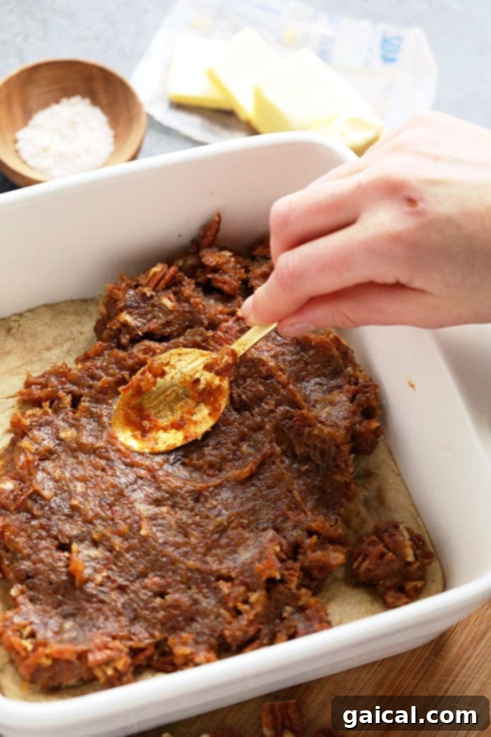 Spreading Date Caramel on Pecan Pie Bar Crust A hand gently spreading the thick, luscious date caramel mixture over the golden almond shortbread crust in a baking pan.