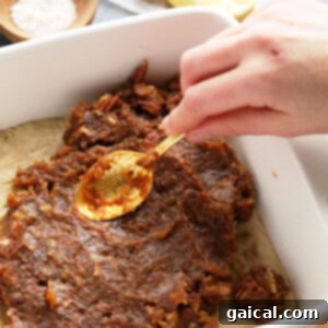 A person effortlessly prepares easy pecan pie bars by pouring a spoonful of pecans into a baking dish with date caramel.