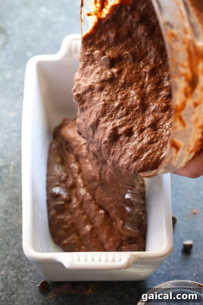 Freshly baked chocolate banana bread cooling in a loaf pan, with a perfectly golden-brown crust.