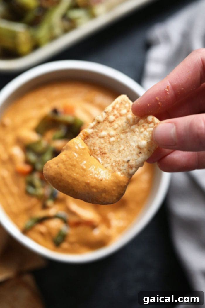 A chip dipped in creamy vegan queso, showcasing its irresistible texture.