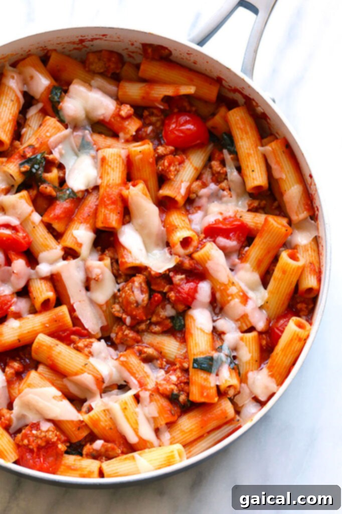 Quick and Easy Sausage Pizza Pasta Simmering in a Skillet Sausage Pizza Pasta simmering in a large cast-iron skillet, showcasing the rich marinara sauce, crumbled cooked sausage, vibrant cherry tomatoes, and perfectly al dente pasta strands, promising a hearty meal.