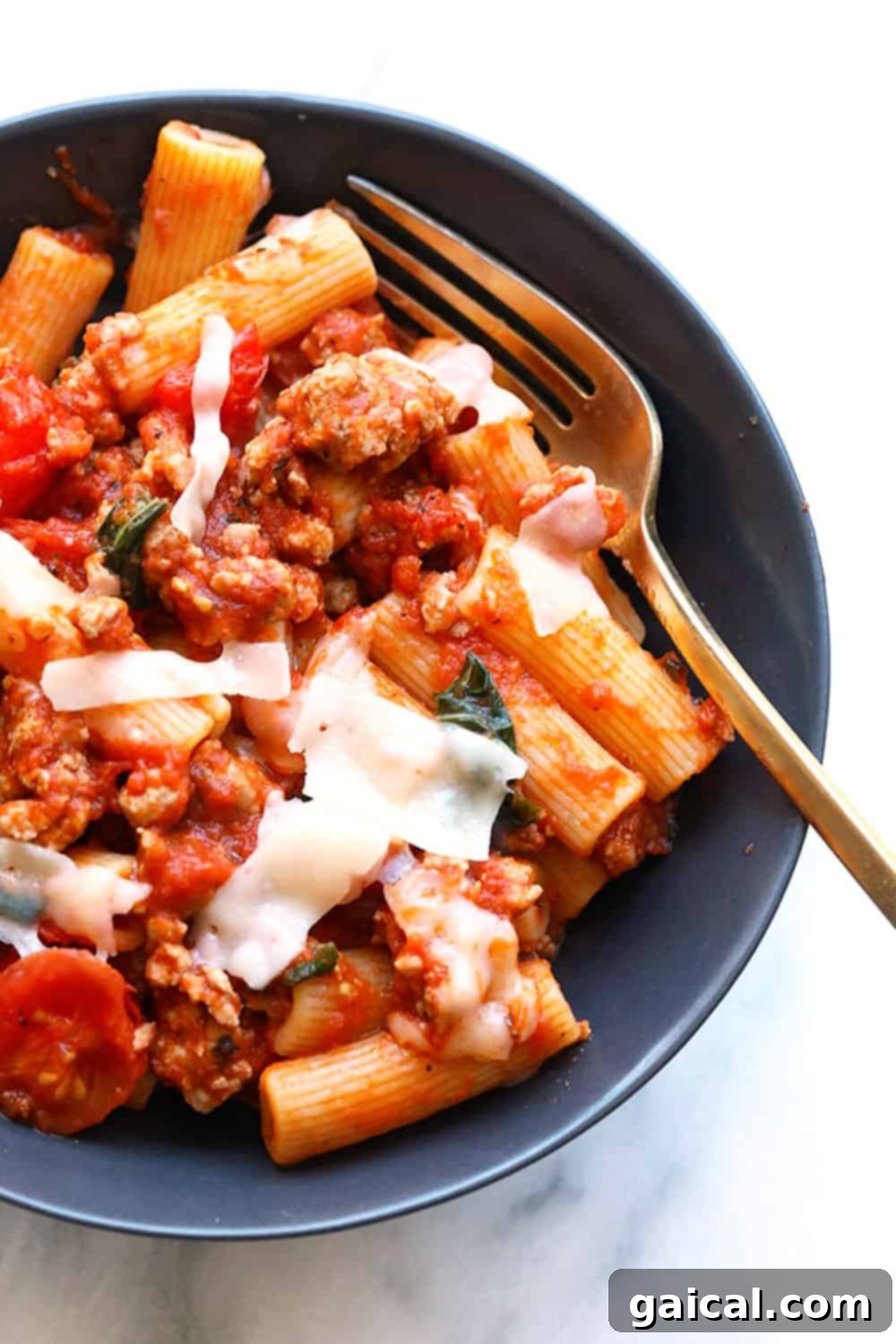 Hearty and Flavorful Sausage Pizza Pasta for a Quick Dinner A vibrant close-up, top-down shot of the finished Sausage Pizza Pasta, showing the creamy, rich texture of the sauce, tender chunks of sausage, halved cherry tomatoes, and fresh basil leaves, generously garnished with shaved Parmesan cheese.