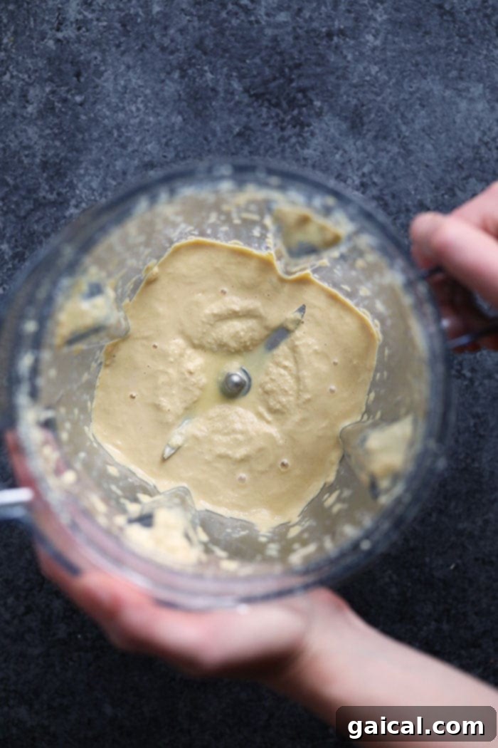 A high-speed blender containing the smooth, creamy cashew cheese sauce ready for mixing.
