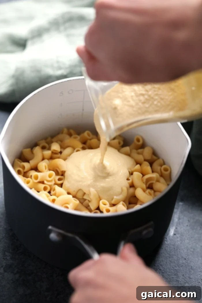 Vegan mac and cheese sauce being poured generously over a pot of cooked noodles.