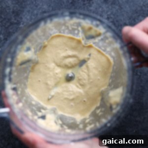 A person is preparing the cashew cream sauce in a blender for vegan mac and cheese.