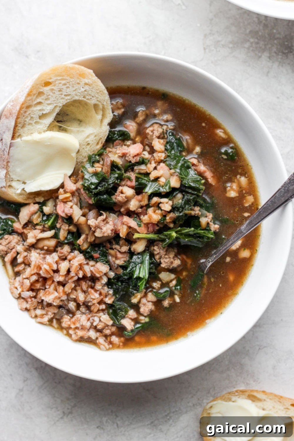 A close-up of a serving of ground turkey farro soup with kale in a rustic bowl, garnished with fresh herbs.