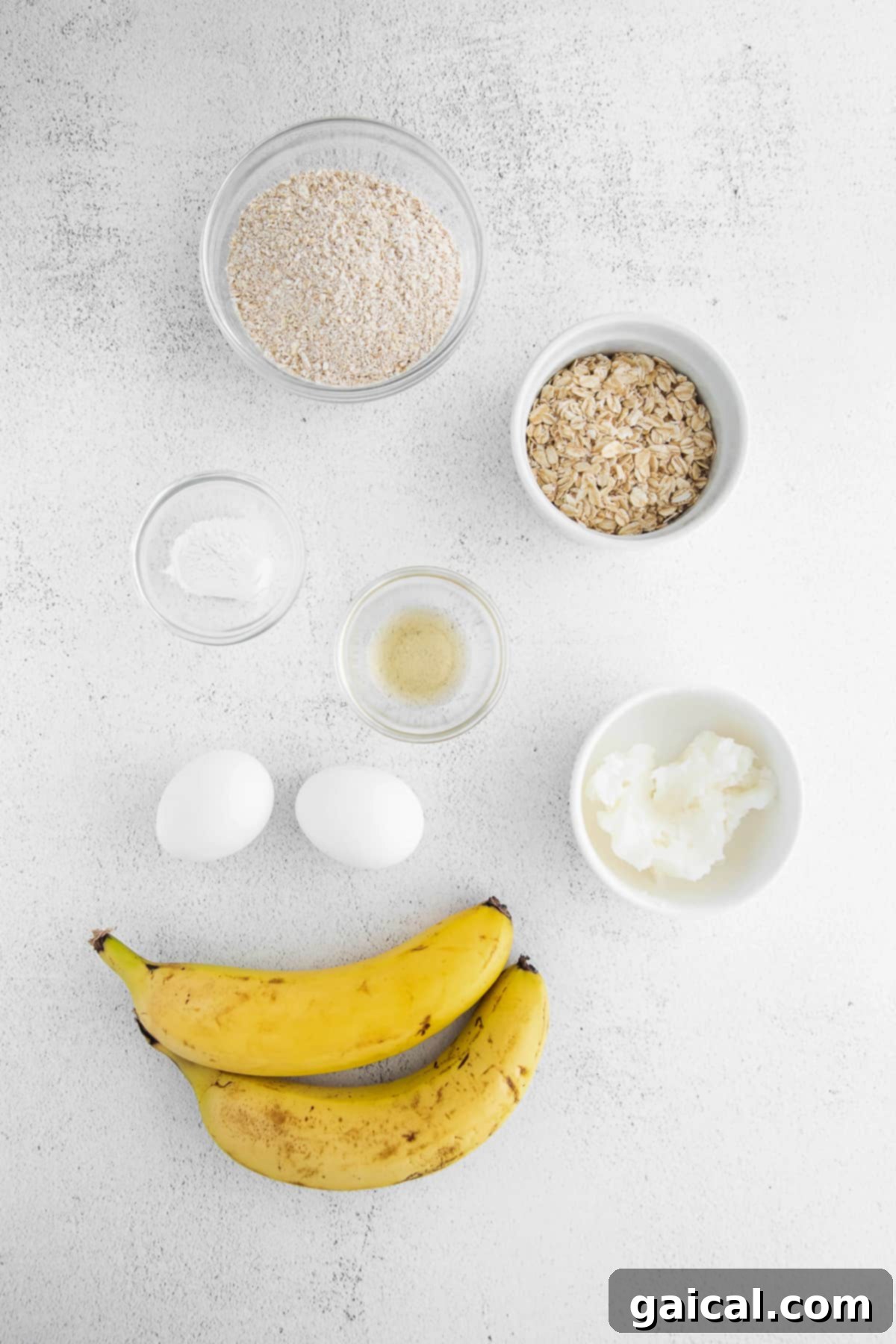 Assortment of fresh ingredients for banana oatmeal pancakes laid out on a kitchen counter: ripe bananas, eggs, coconut oil, rolled oats, and vanilla extract.