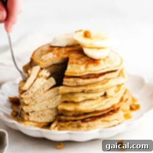 Stack of fluffy banana pancakes on a plate, garnished with fresh banana slices.