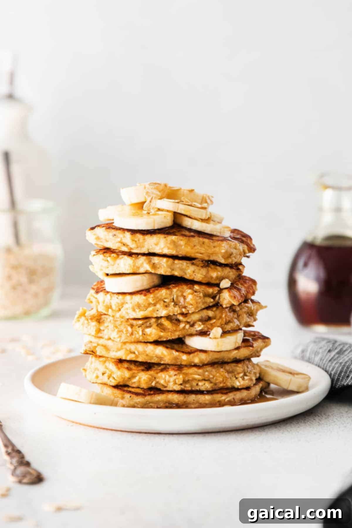 A beautifully plated stack of banana oatmeal pancakes topped with fresh banana slices, oats, and a drizzle of maple syrup.
