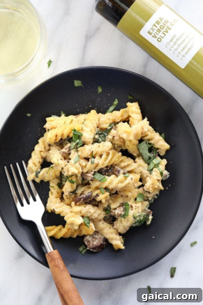 Deliciously creamy vegan pasta bake with white wine cashew sauce, garnished with fresh herbs, served on a white plate, highlighting its rich texture and vibrant ingredients.