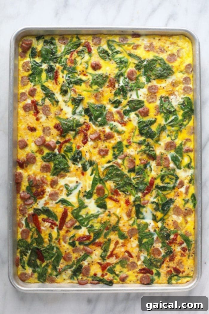 Cooked egg patty with vegetables and sausage on a sheet pan, ready for slicing.