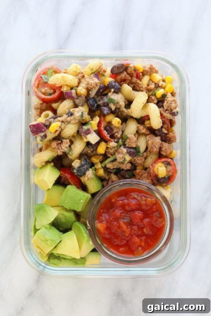 What happens when you merge taco salad and pasta salad?! You get an epic taco pasta salad. Good news, though! This is a healthy taco pasta salad that doesn't sacrifice flavor one bit. Meal prep container featuring taco pasta salad, perfectly portioned with avocado slices and salsa on the side