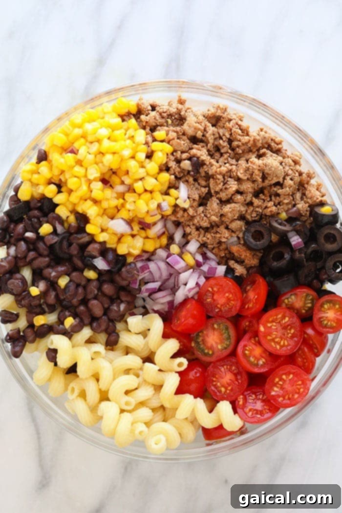 Healthy taco pasta salad made with ground turkey, your favorite noodle, and all the taco fixings! Close-up of healthy taco pasta salad in a clear glass bowl, showcasing fresh ingredients