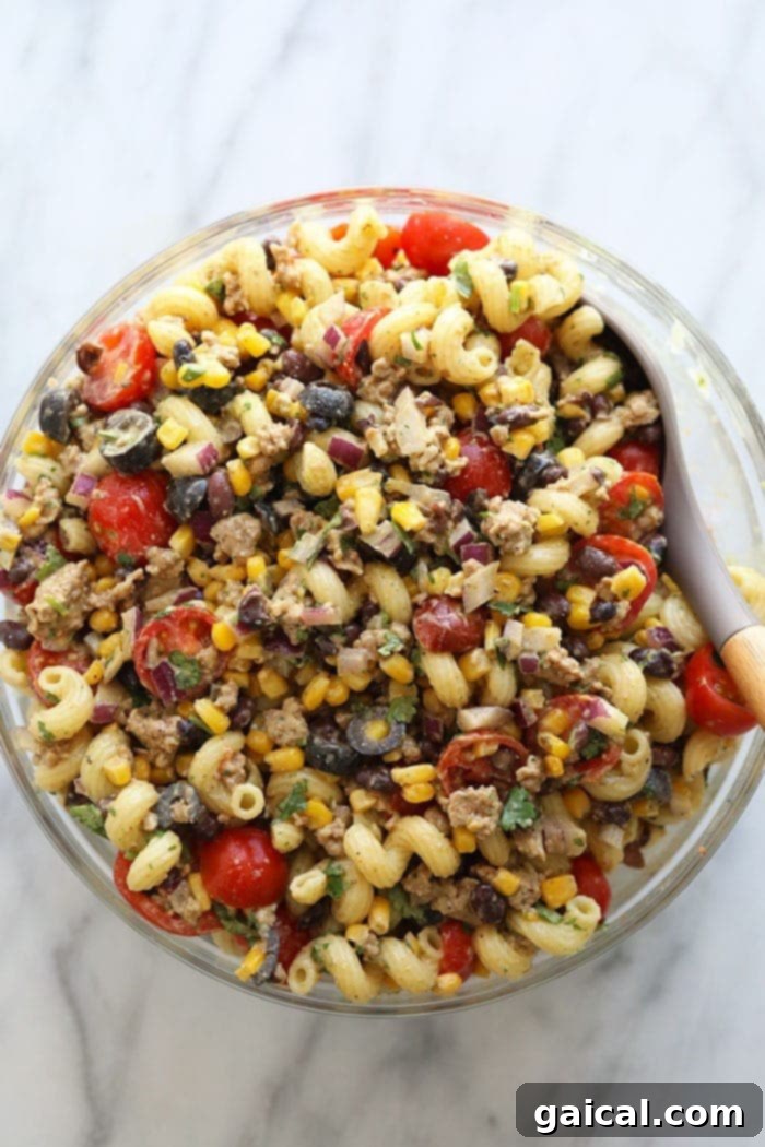 This healthy taco pasta salad is made with your favorite pasta, your favorite ground meat, a yummy cilantro lime dressing, and tons of veggies! Large bowl of healthy taco pasta salad, garnished beautifully with fresh herbs and a lime wedge