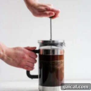 Mastering the French Press 11 A hand pressing down the plunger of a French press, separating grounds from brewed coffee.