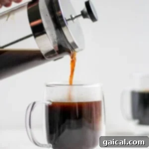 Mastering the French Press 12 A person pouring a rich, dark stream of French press coffee into a clear glass mug.