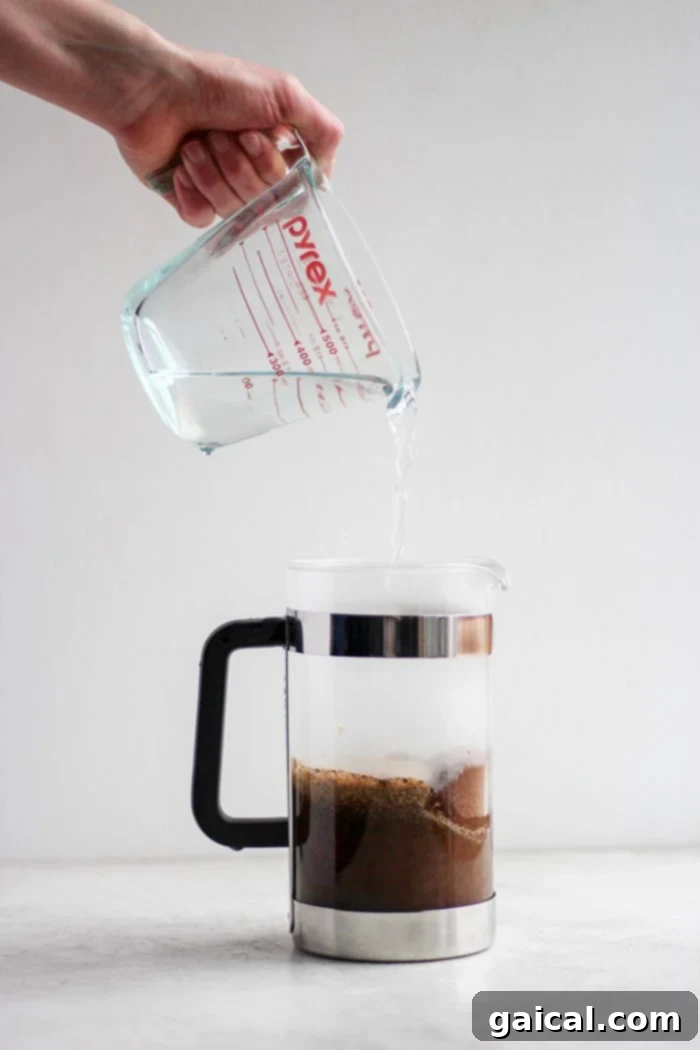 Mastering the French Press 5 Pouring hot water from a kettle into a French press filled with coffee grounds.