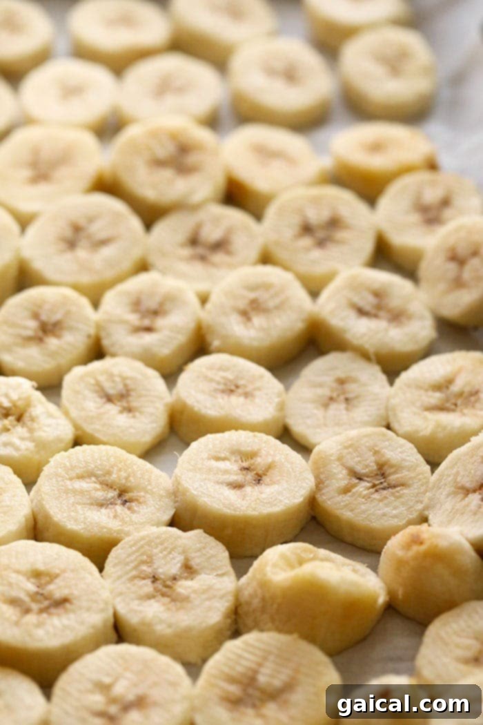 Individually Frozen Banana Slices A close-up view of firm, individually frozen banana slices on a baking sheet after flash freezing
