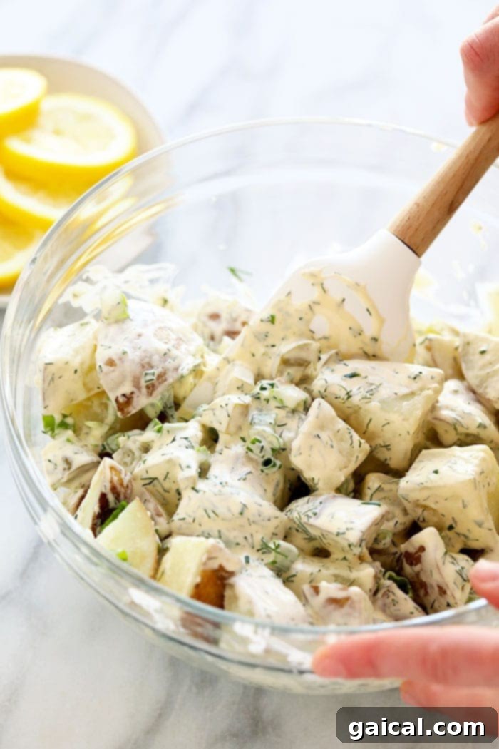 A hand gently mixing a vibrant vegan potato salad in a large bowl, showcasing the creamy dressing and fresh green herbs.