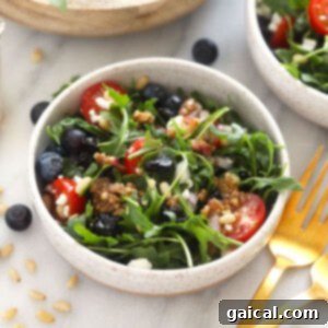 A beautifully arranged bowl of healthy salad, featuring fresh greens, berries, and nuts.