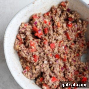 A white bowl with a black bean burger and peppers.