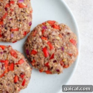 Three black bean burgers topped with red peppers and onions on a plate.