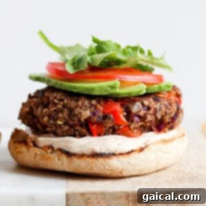 A black bean burger with lettuce, tomatoes and avocado on a cutting board.