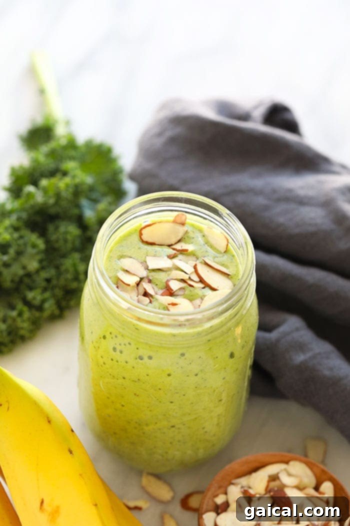 Get your daily greens here! This is the most delicious kale smoothie you'll ever make! It's packed with nutrient dense kale, frozen bananas and the perfect flavor punch of orange juice and fresh ginger. Whip up this green smoothie in 5 minutes and you're off and running with a healthy breakfast or snack on the go. A vibrant kale smoothie served in a clear mason jar, topped with a straw, showcasing its healthy green color.