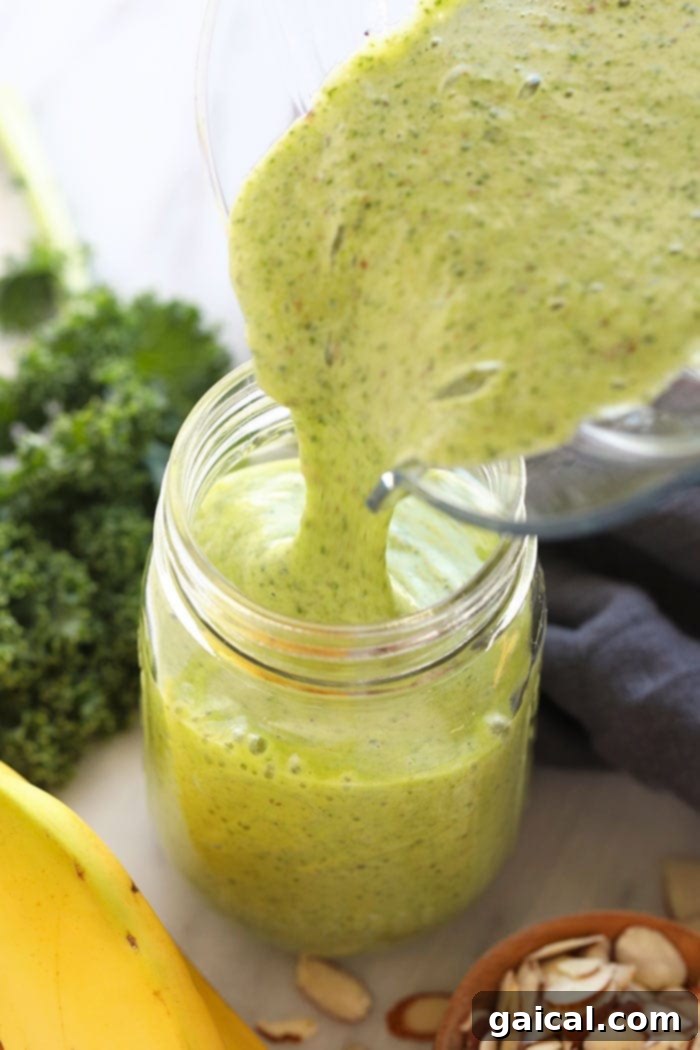Get your daily greens here! This is the most delicious kale smoothie you'll ever make! It's packed with nutrient dense kale, frozen bananas and the perfect flavor punch of orange juice and fresh ginger. Whip up this green smoothie in 5 minutes and you're off and running with a healthy breakfast or snack on the go. A freshly blended kale smoothie being poured from a high-speed blender into a mason jar.